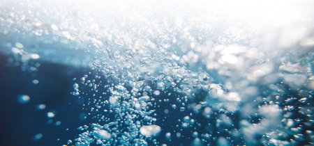 Underwater view with numerous rising air bubbles, illuminated by light from above, creating a dynamic and refreshing scene.