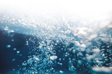 Underwater view with numerous rising air bubbles, illuminated by light from above, creating a dynamic and refreshing scene.