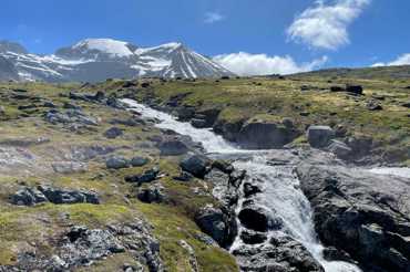 Mountain stream flowing over rocks with snow-covered peaks in the background