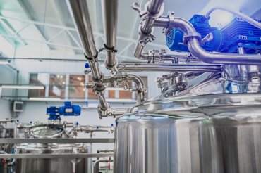 Industrial stainless steel processing equipment with pipes and motors in a factory setting.