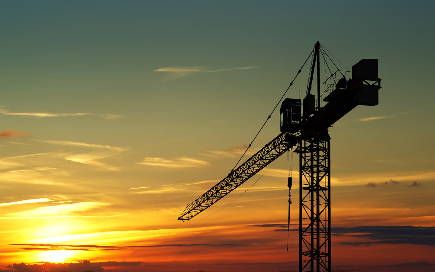 A large construction crane silhouetted against a colorful sunset sky with hues of orange, yellow, and blue.