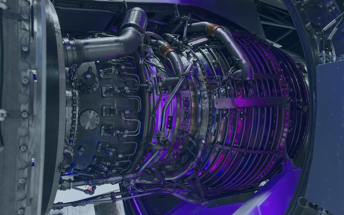 Close-up view of a high-tech jet engine with intricate metallic components and pipes, illuminated by purple lighting.