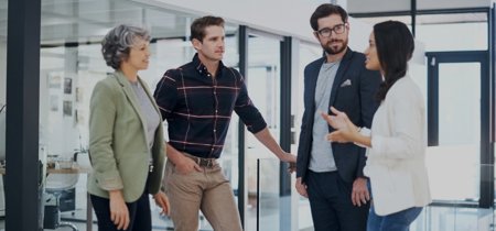 Four colleagues talking in a modern office environment.